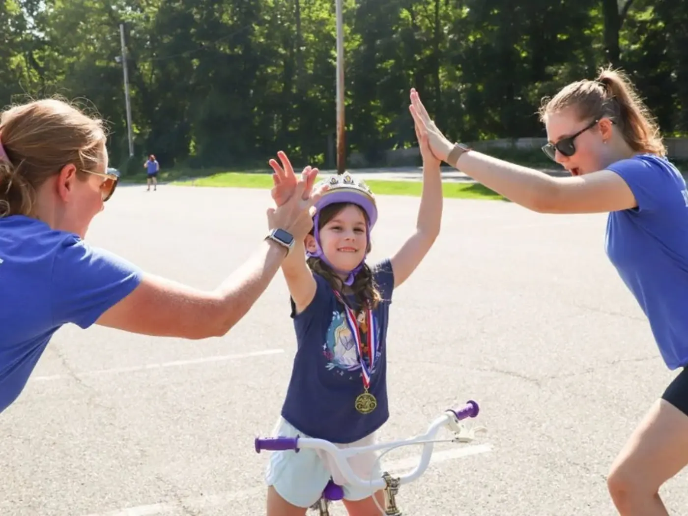 A child on a bike high-fiving two Ready to Pedal instructors